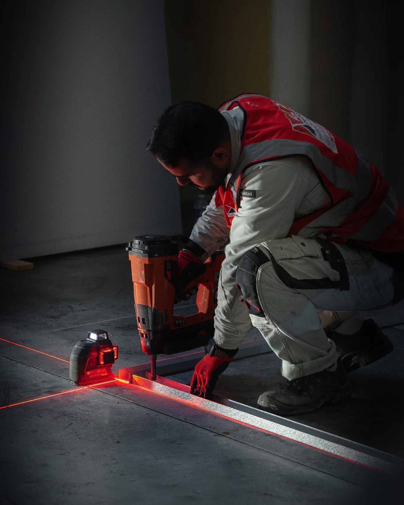 Un plaquiste ALP fixe une ossature au sol en suivant les repères d’un niveau laser.